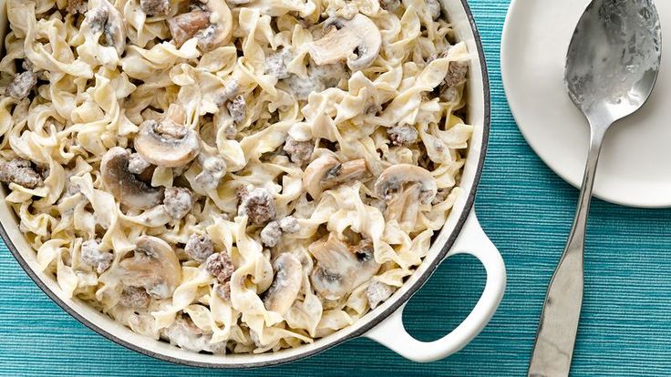 a pot filled with pasta and mushrooms on top of a blue table cloth next to a plate