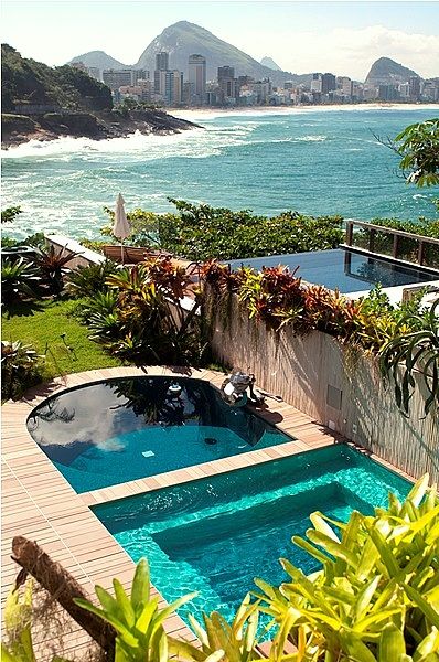 an outdoor swimming pool surrounded by greenery next to the ocean with mountains in the background