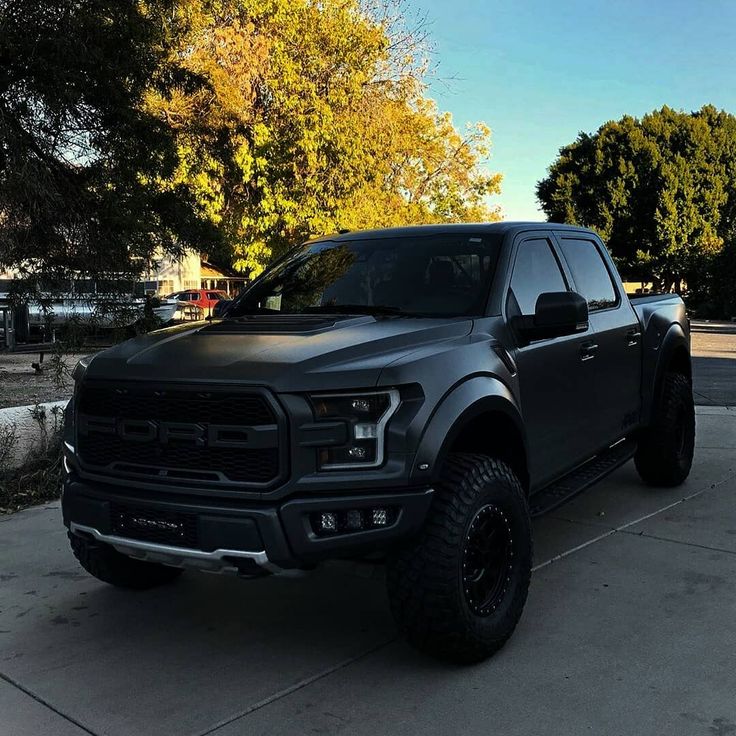 a black truck is parked on the side of the road in front of some trees