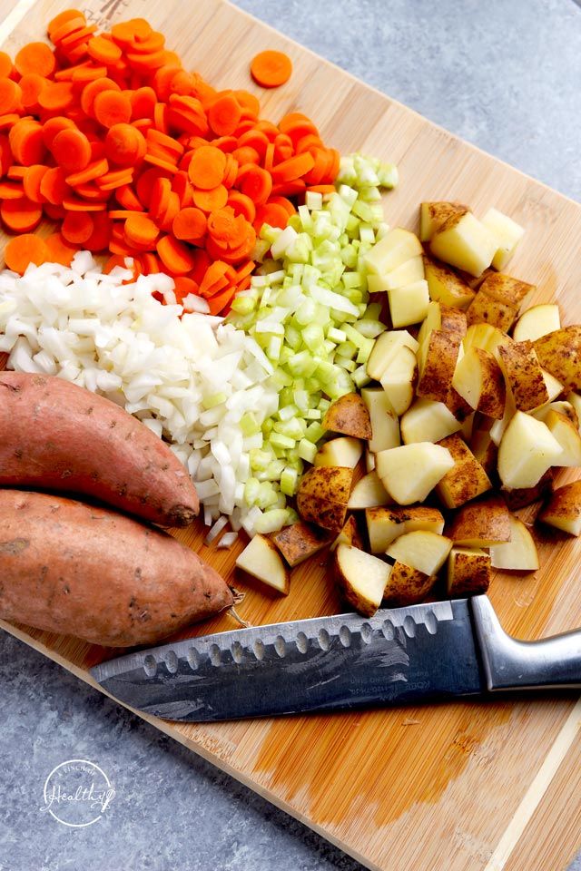 chopped potatoes, carrots, and other vegetables on a cutting board with a knife