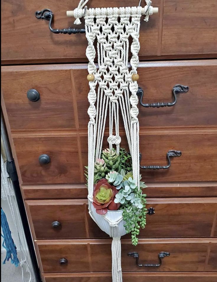 a white macrame hanging from a dresser with succulents and other plants