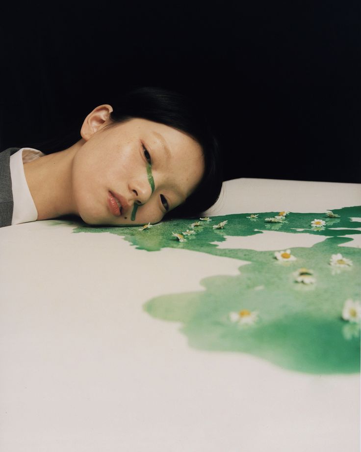 a woman laying on top of a bed with her head resting on the table next to flowers