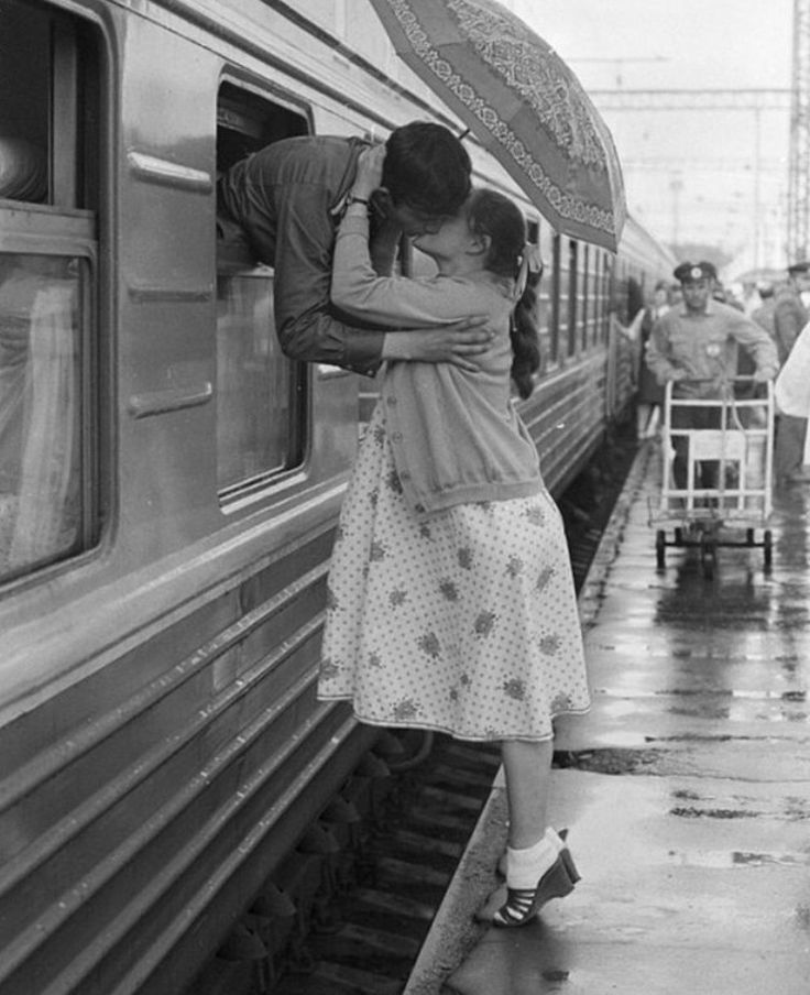 a black and white photo of people standing on the side of a train with an umbrella