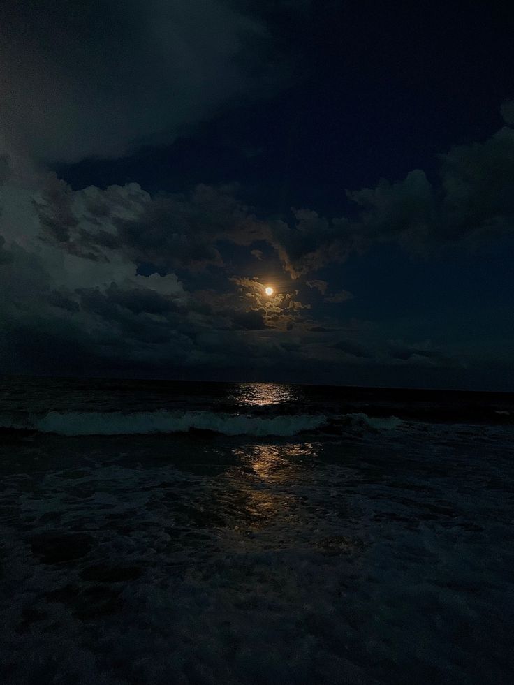 the full moon shines brightly in the dark night sky over the ocean with waves