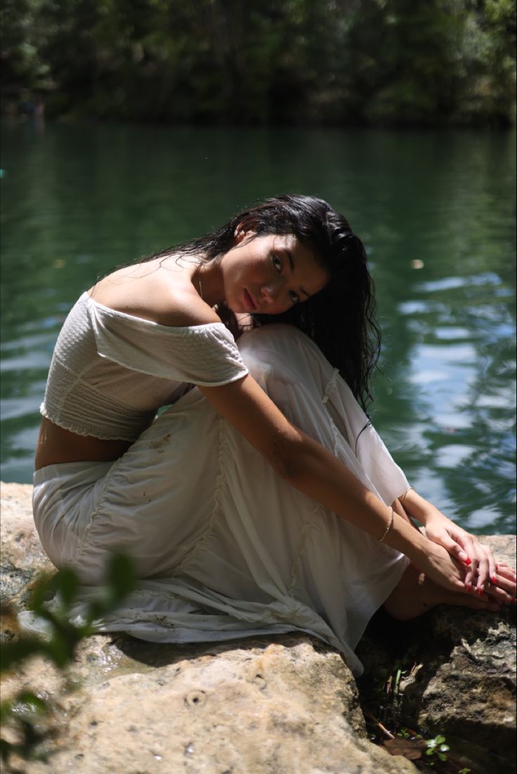 a woman sitting on top of a rock next to water