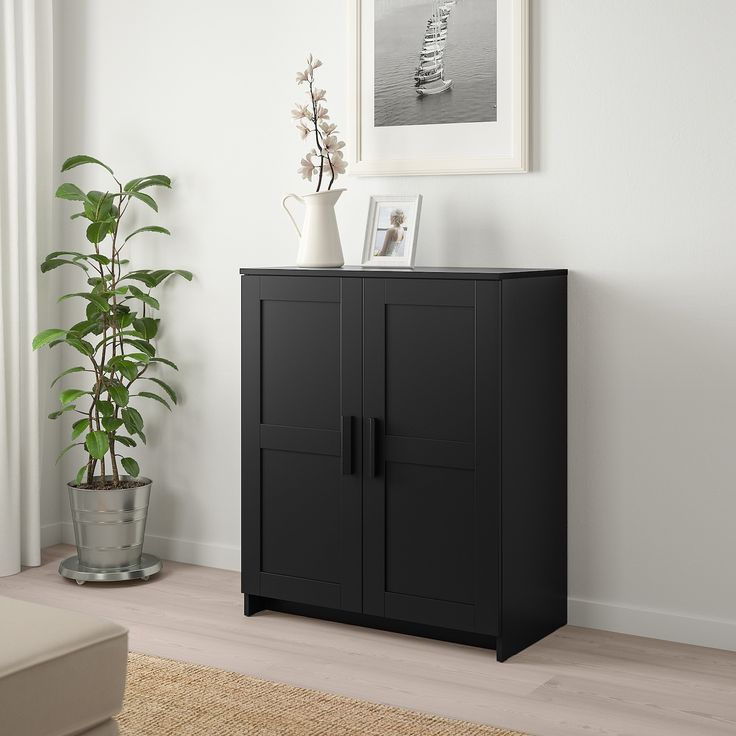 a black cabinet sitting next to a potted plant in a living room with white walls