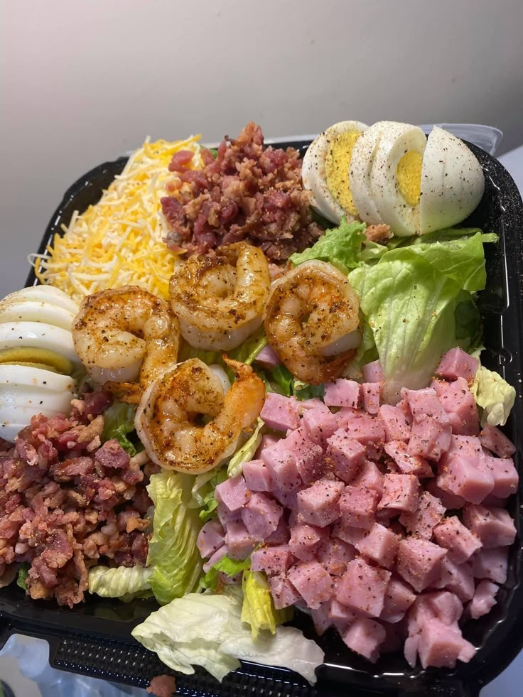 a plastic container filled with salad and meats next to hard boiled eggs on top of lettuce