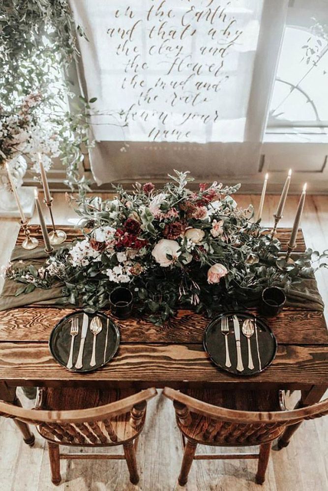 a wooden table topped with flowers and candles next to two chairs in front of a window