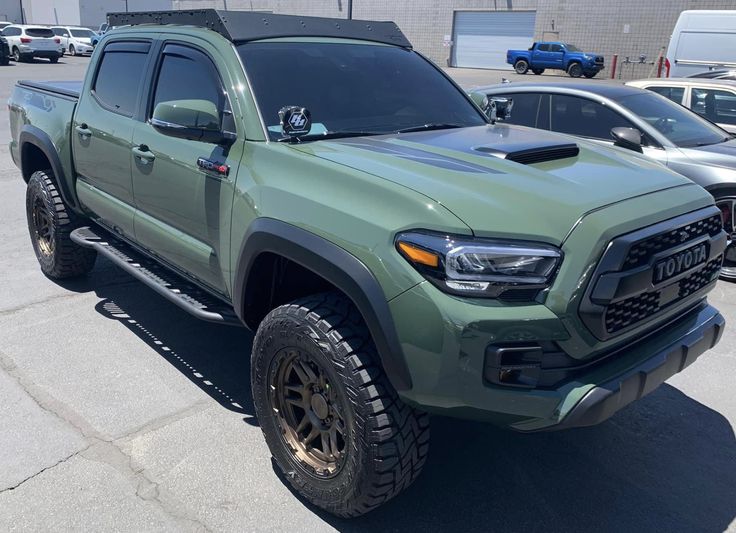 a green truck parked in a parking lot next to other cars and trucks behind it