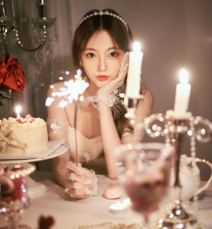 a woman sitting at a table in front of a cake with lit candles on it