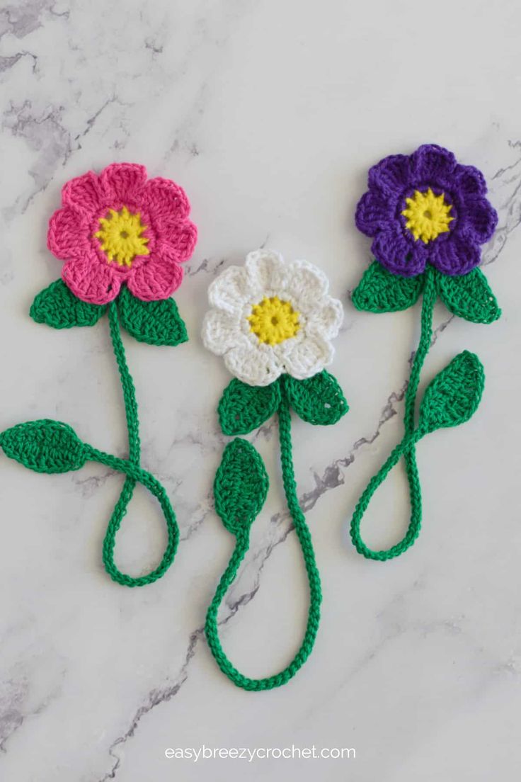 three crocheted flowers sitting on top of a marble counter