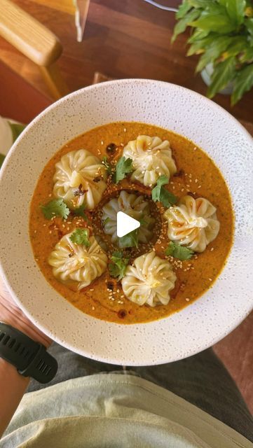 a bowl of soup with dumplings and garnishes in it on a table