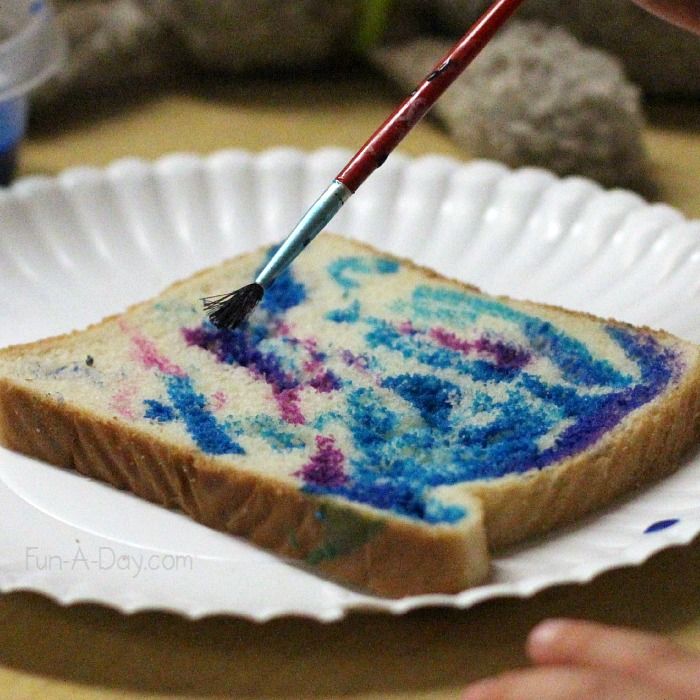 someone using a paint brush to decorate a piece of bread with blue and pink sprinkles