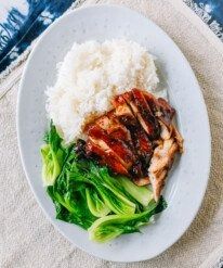 a white plate topped with meat and vegetables next to rice on a blue table cloth