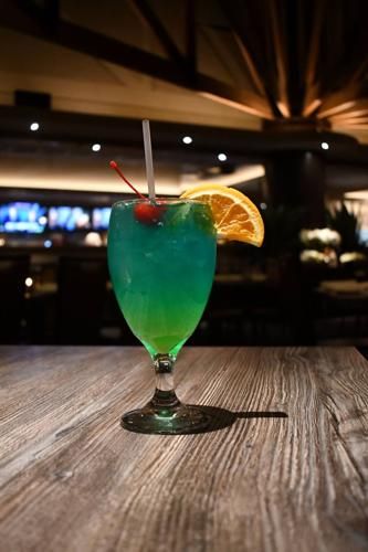 a green and blue drink sitting on top of a wooden table next to a bar