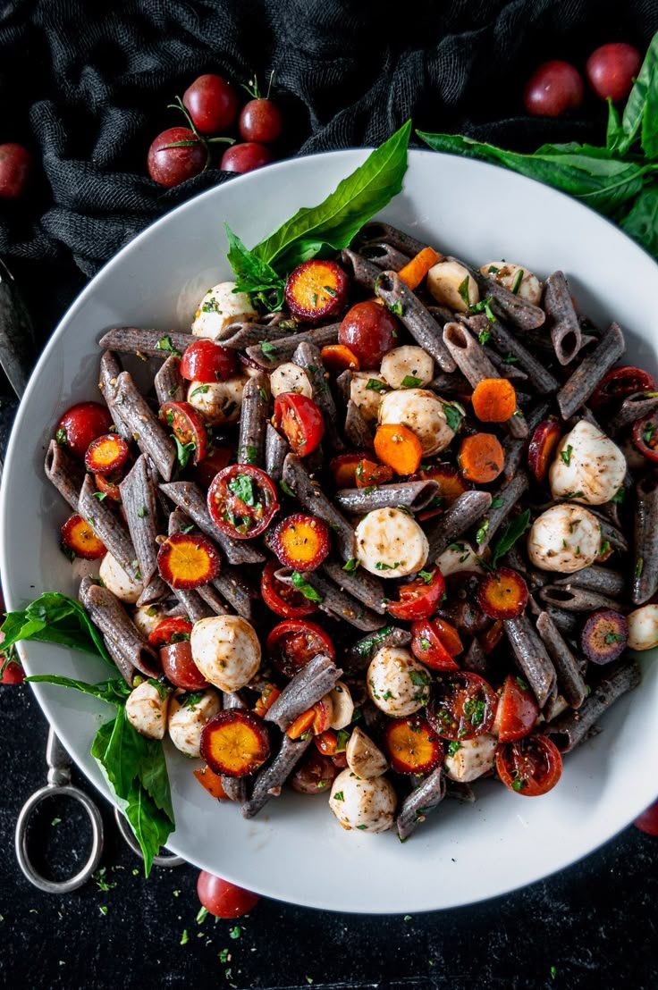 a white bowl filled with pasta and vegetables on top of a black table next to tomatoes