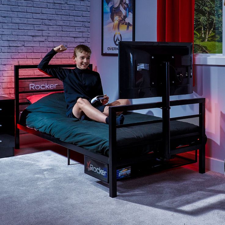 a young boy sitting on top of a bed next to a tv