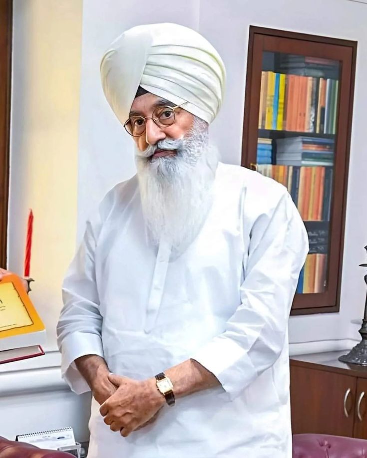 an old man with a white turban standing in front of a bookshelf