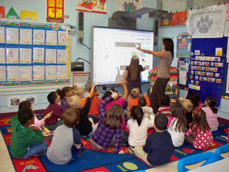 there is a woman teaching to children in a classroom at the same time as they sit on the floor