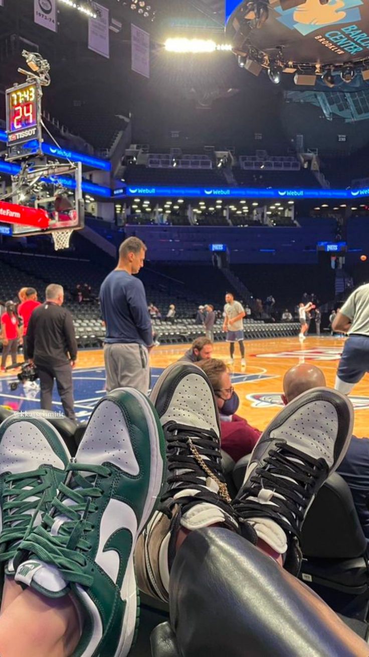 people are sitting on the floor at a basketball game with their feet up in the air