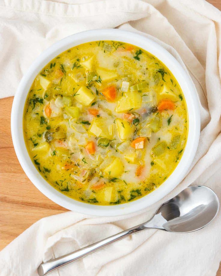 a white bowl filled with vegetable soup on top of a wooden table next to a spoon