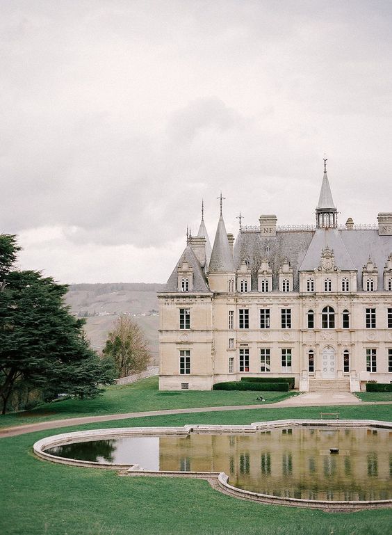 a large castle like building sitting on top of a lush green field next to a pond