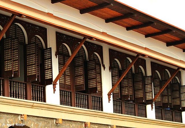 a clock is on the side of a building with wooden balconies and arched windows