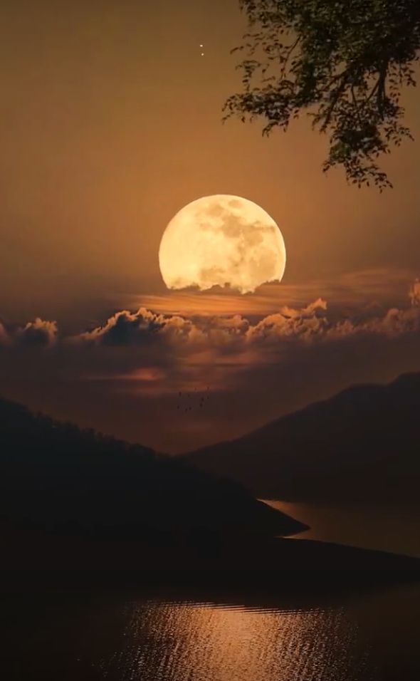 the full moon is setting over water and mountains