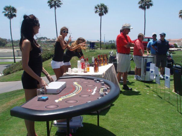 several people standing around a table with drinks and cards on it in front of palm trees