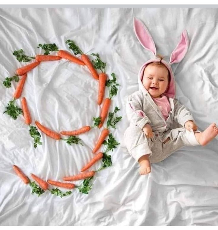 a baby wearing bunny ears sitting next to carrots