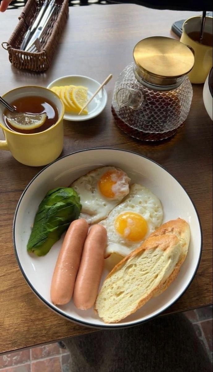 a plate with eggs, sausages and bread on it sitting on a table next to tea