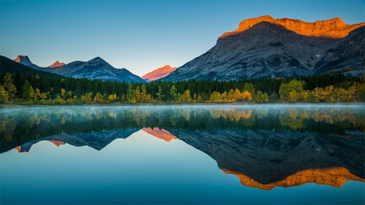 the mountains are reflected in the still waters of this mountain lake at sunrise or sunset