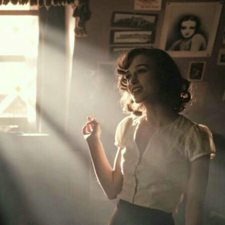 a woman standing in front of a window with sunlight coming through the blinds on her