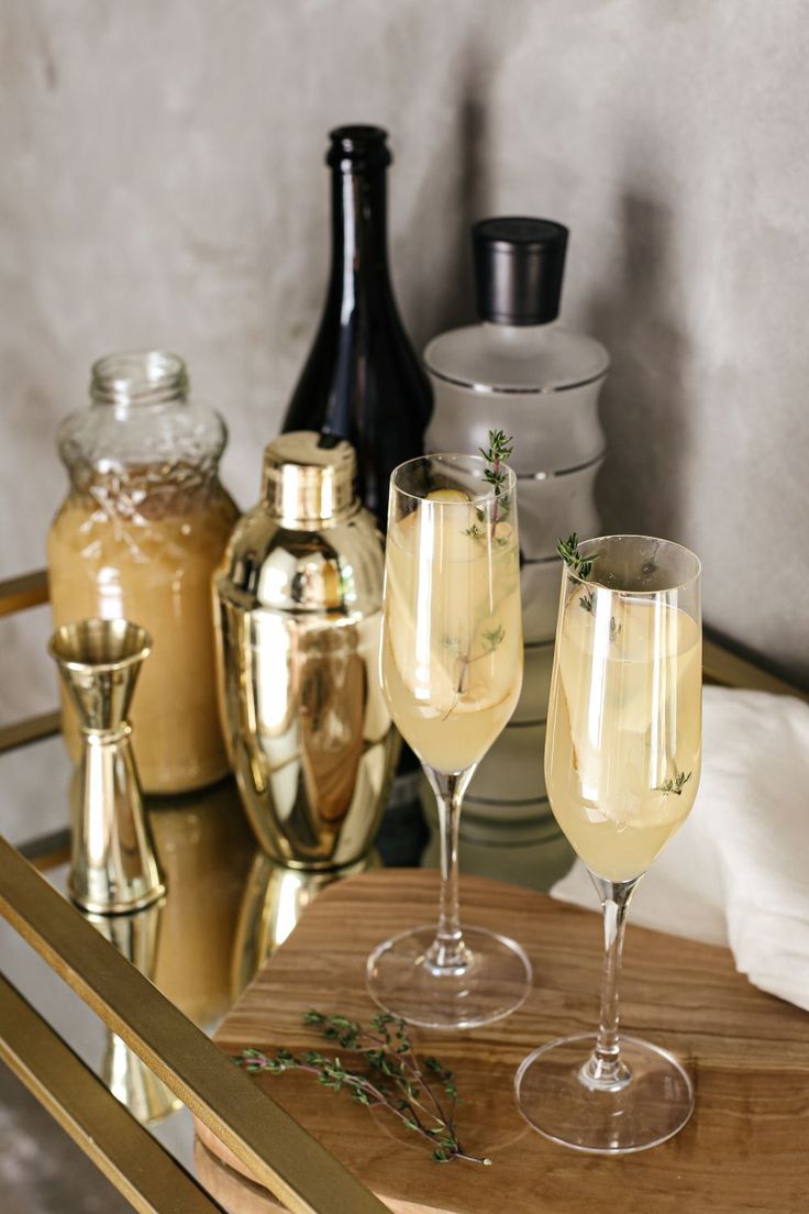 two champagne flutes sitting on top of a wooden table next to bottles and glasses filled with liquid