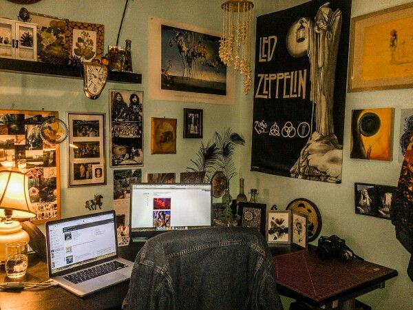 a laptop computer sitting on top of a wooden desk in front of a wall covered with pictures