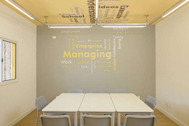 an empty conference room with white tables and chairs in front of a wall that has words written on it