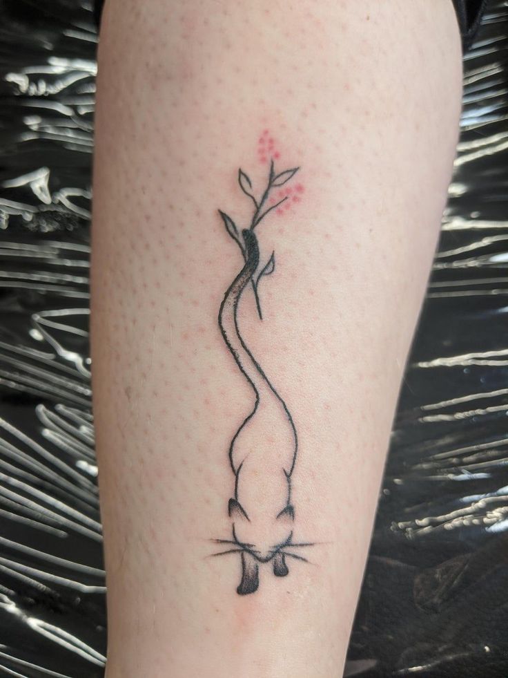 a tattoo on the leg of a woman with a cat and plant growing out of it