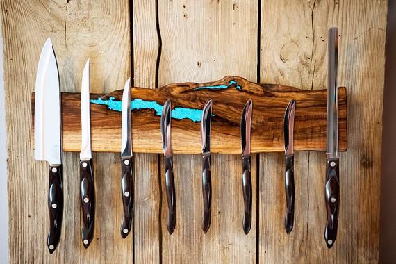 five knives are hanging on a wooden rack with blue paint in the center and black handles