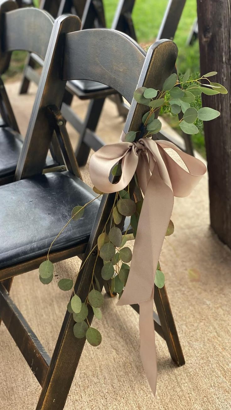 a row of wooden chairs with ribbons tied around the back of them and eucalyptus leaves on each chair