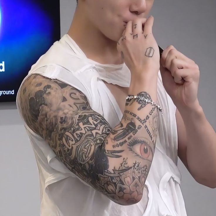 a man with tattoos on his arm and hand covering his mouth while standing in front of a tv screen