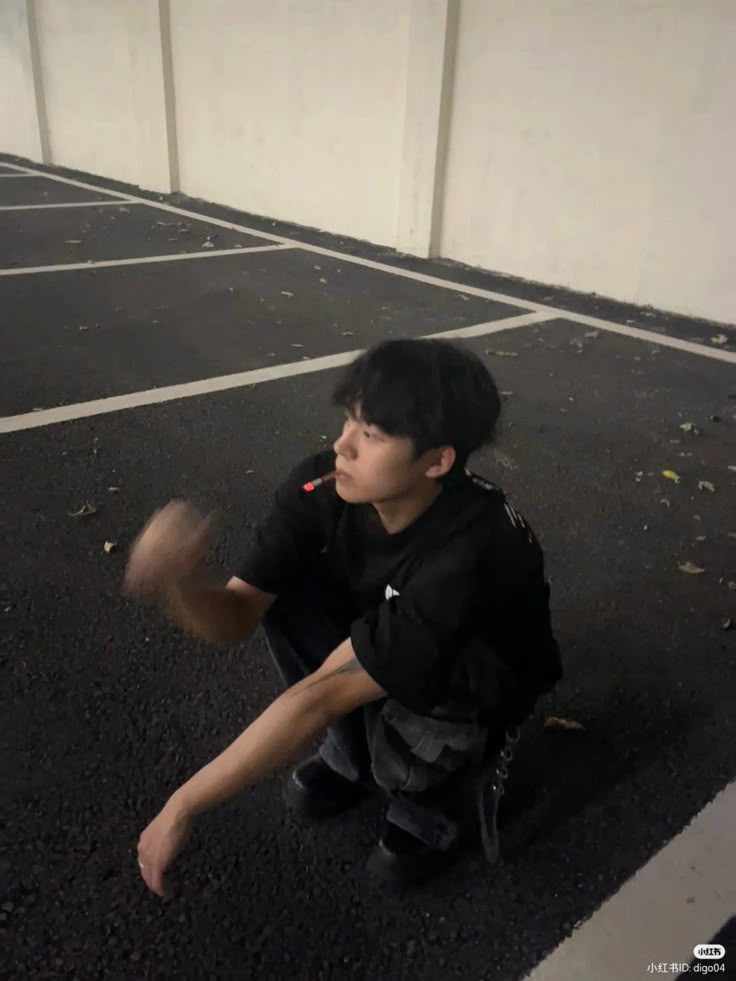 a young boy sitting in the middle of an empty parking lot holding a baseball bat