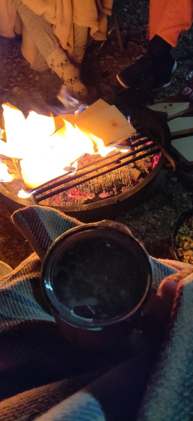 a person is cooking on a grill with flames in front of them and blankets around the fire pit