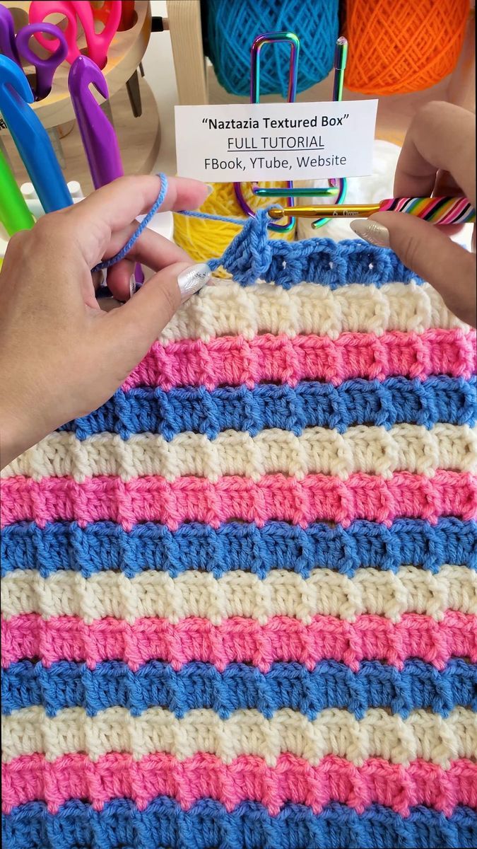 someone is crocheting a striped blanket with scissors and yarn in front of them