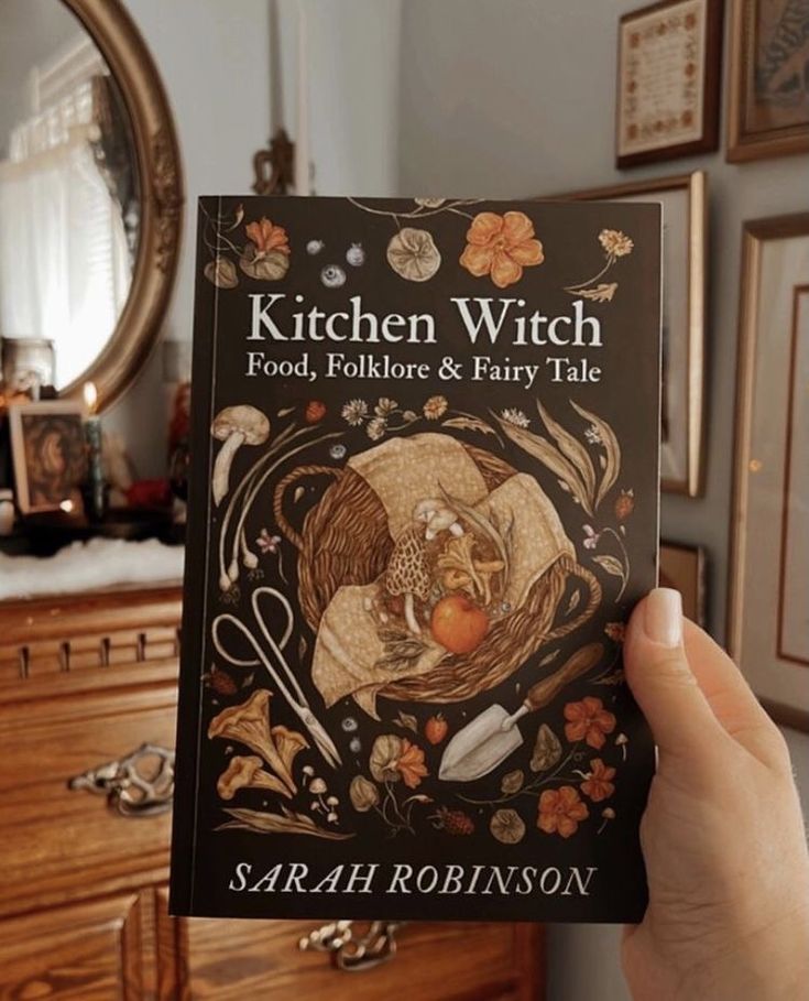 a person holding up a book about kitchen witch food, folklore and fairy tale in their hand