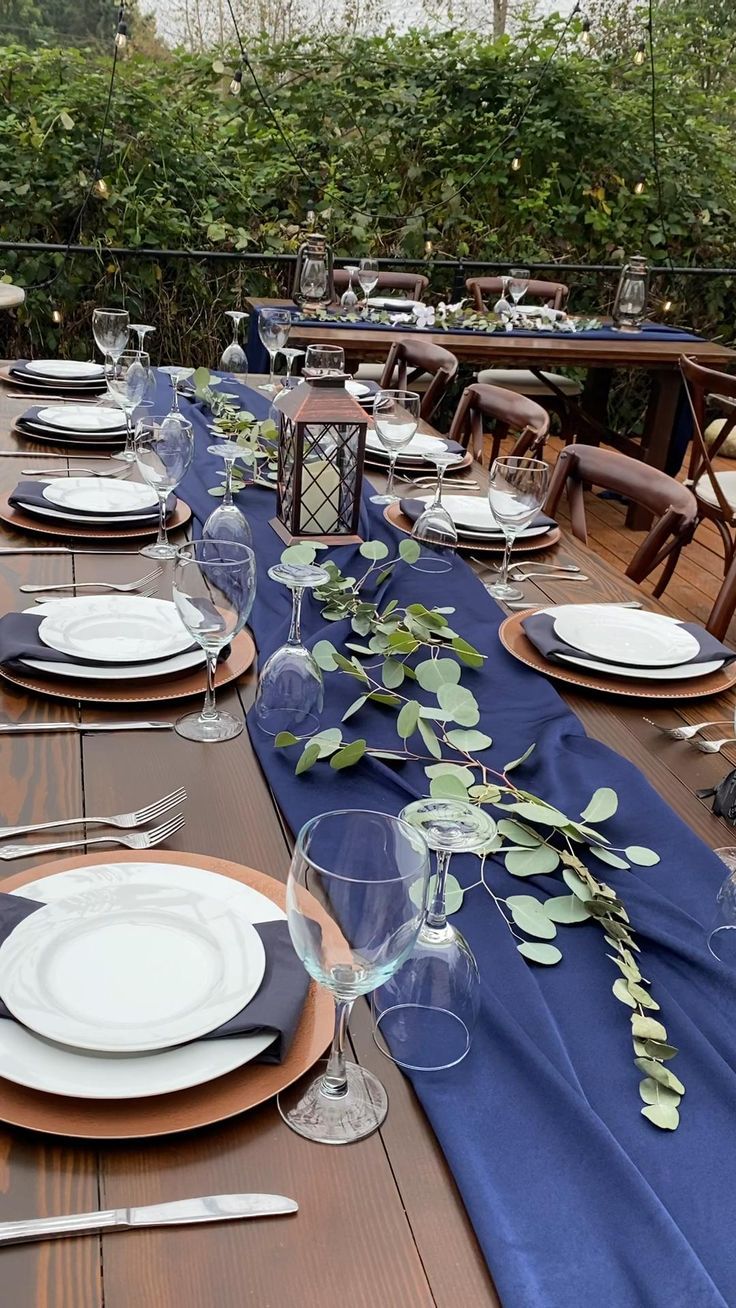 a long table set with plates and silverware on top of a blue cloth covered table