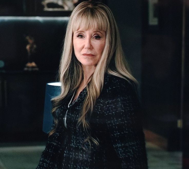 a woman with long blonde hair standing in front of a table holding a coffee cup