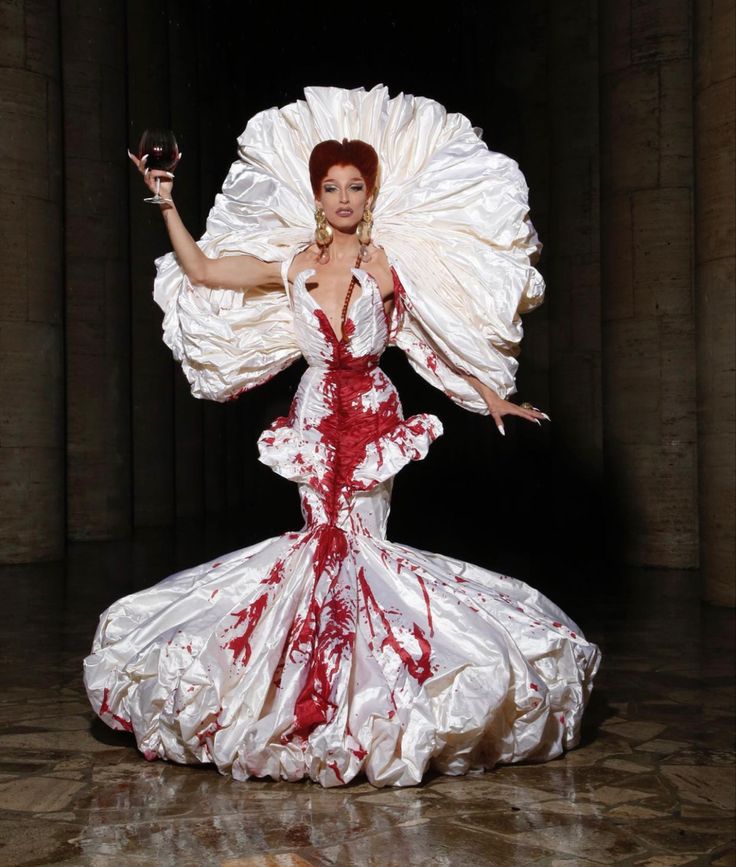 a woman in a white and red dress holding a wine glass with her arms outstretched