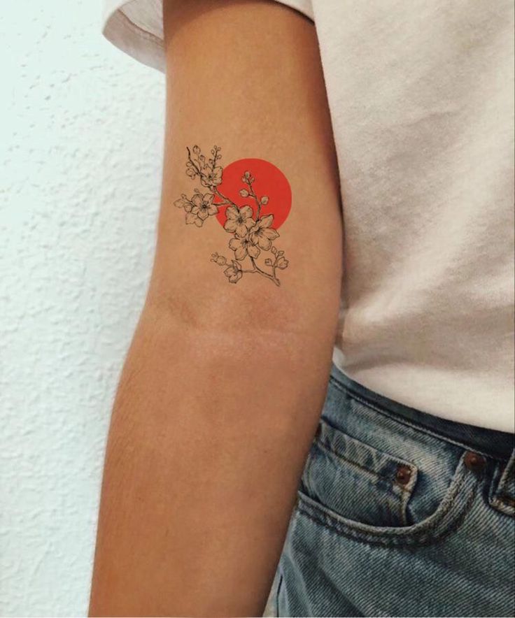 a woman's arm with a tattoo on it that has flowers and an orange sun in the background