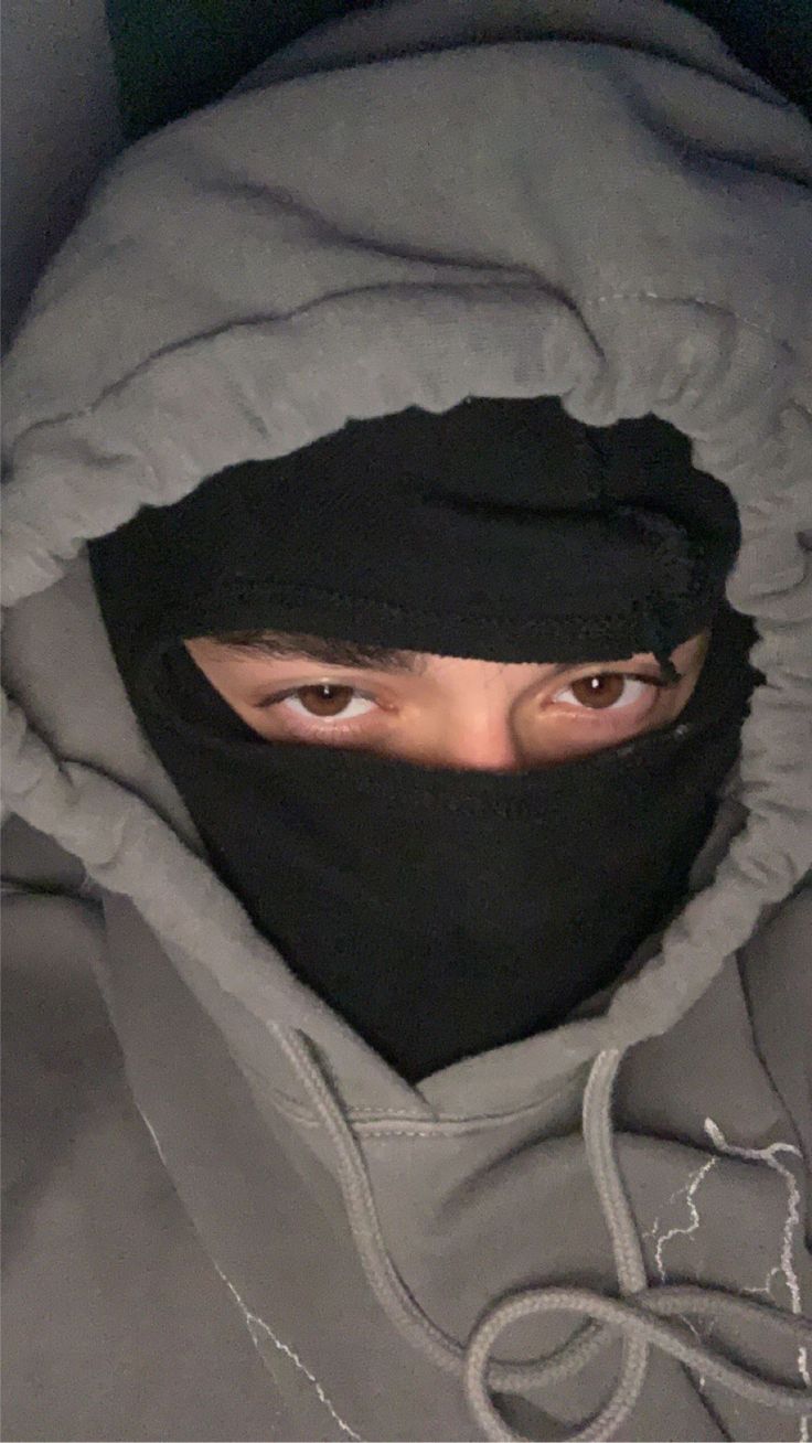 a person wearing a hoodie and covering their face with a black mask