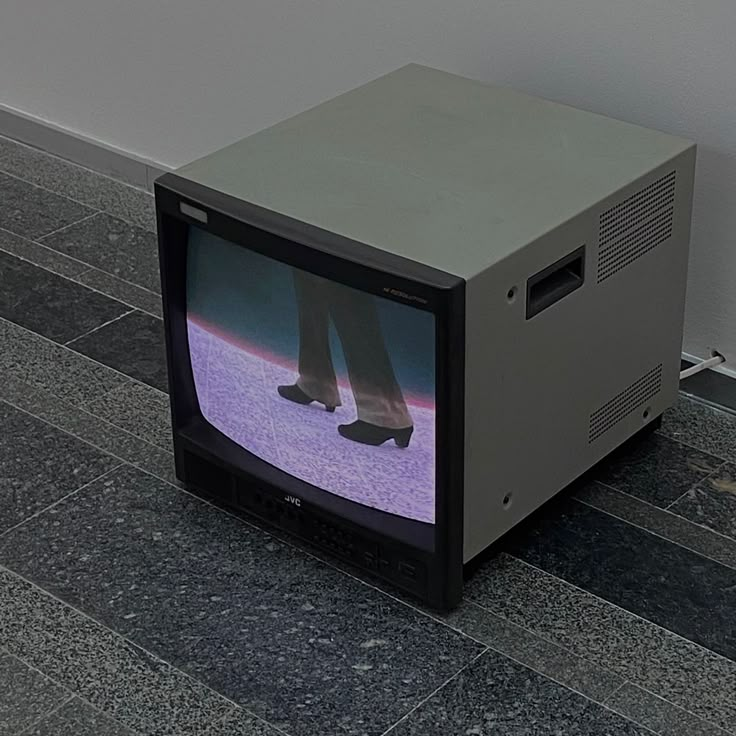 an old tv sitting on the ground with someone's feet in it